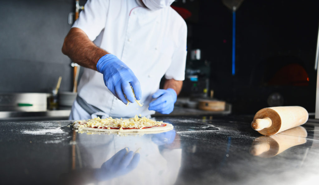 chef  with protective coronavirus face mask preparing pizza