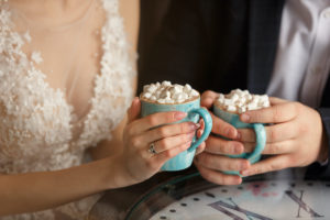 Wedding in winter weather. Bride and groom holding cups of coffee with marshmallows.